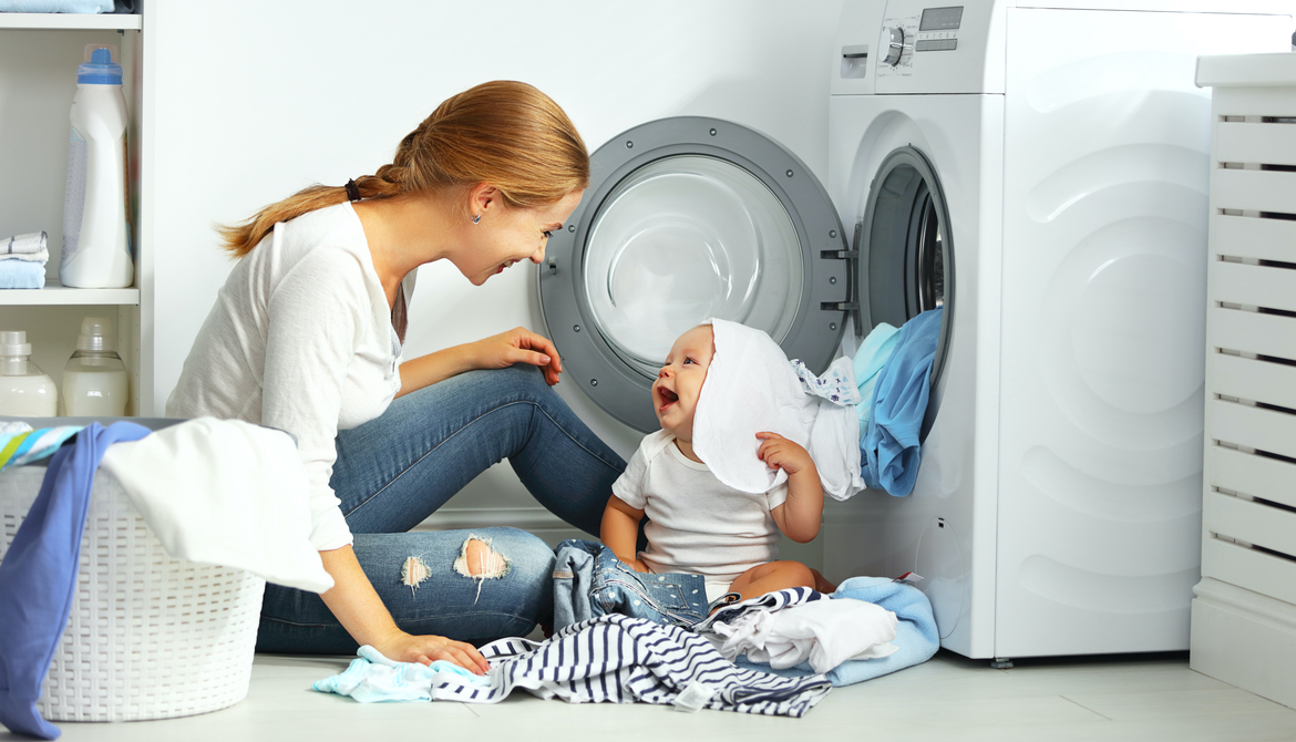 mother a housewife with a baby engaged in laundry fold clothes into the washing machine