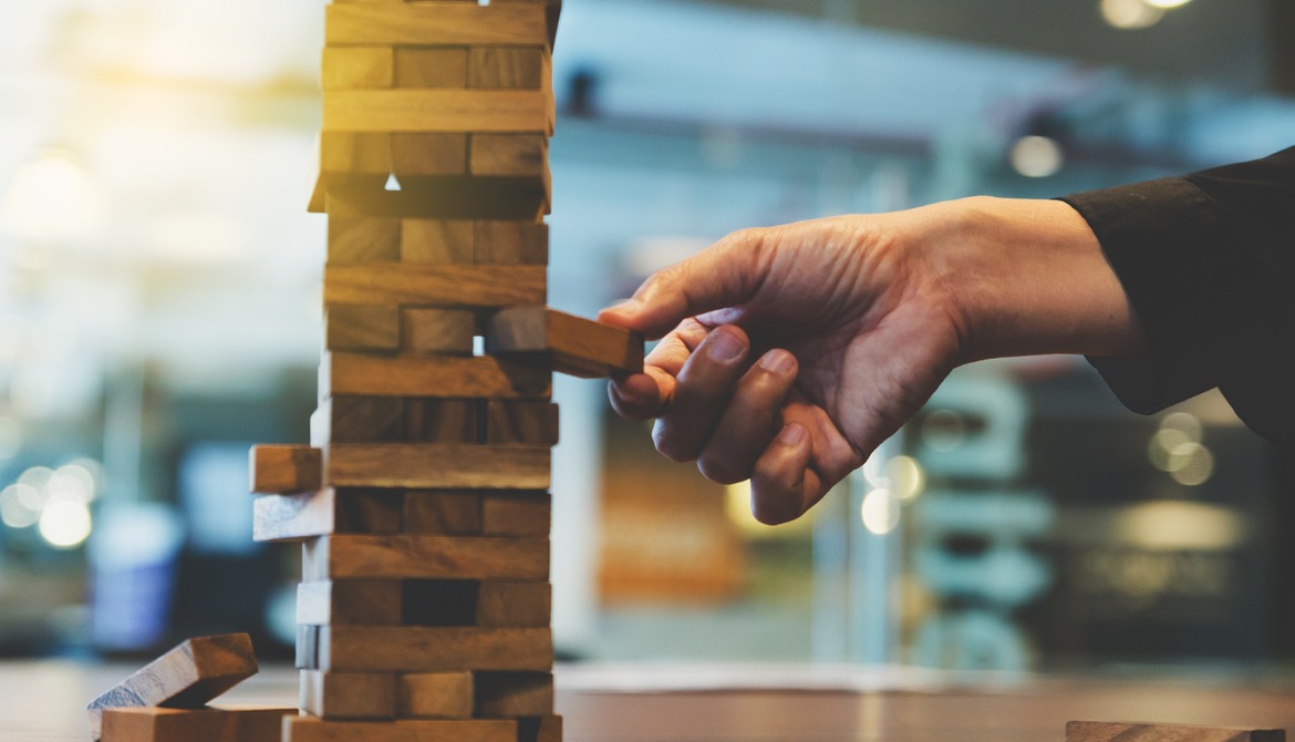 businessperson’s hand reaching out to place or pull a wooden block from a Jenga game tower