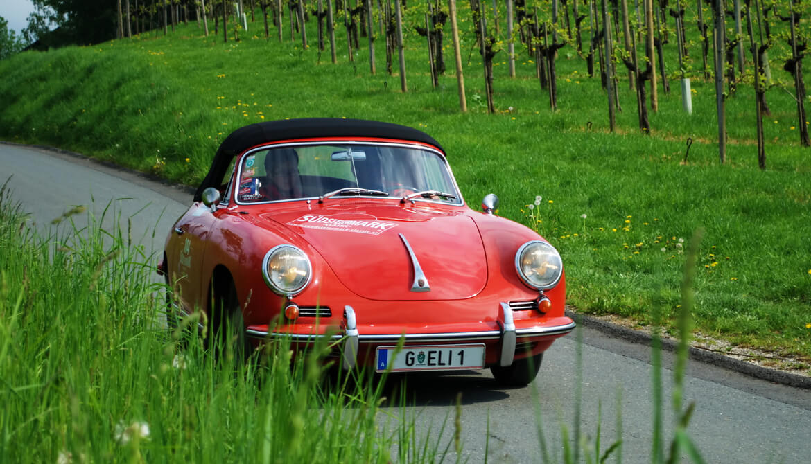 a vintage red Porsche drives along a country highway