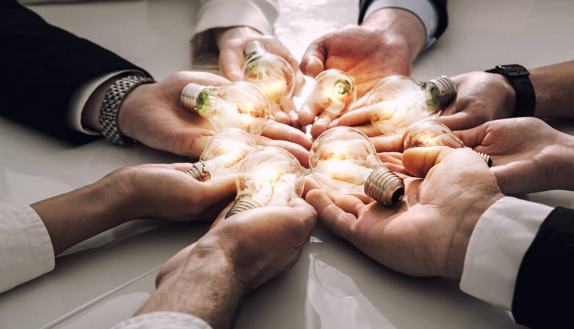 group of business people’s hands holding out glowing lightbulbs to represent team brainstorming and innovation