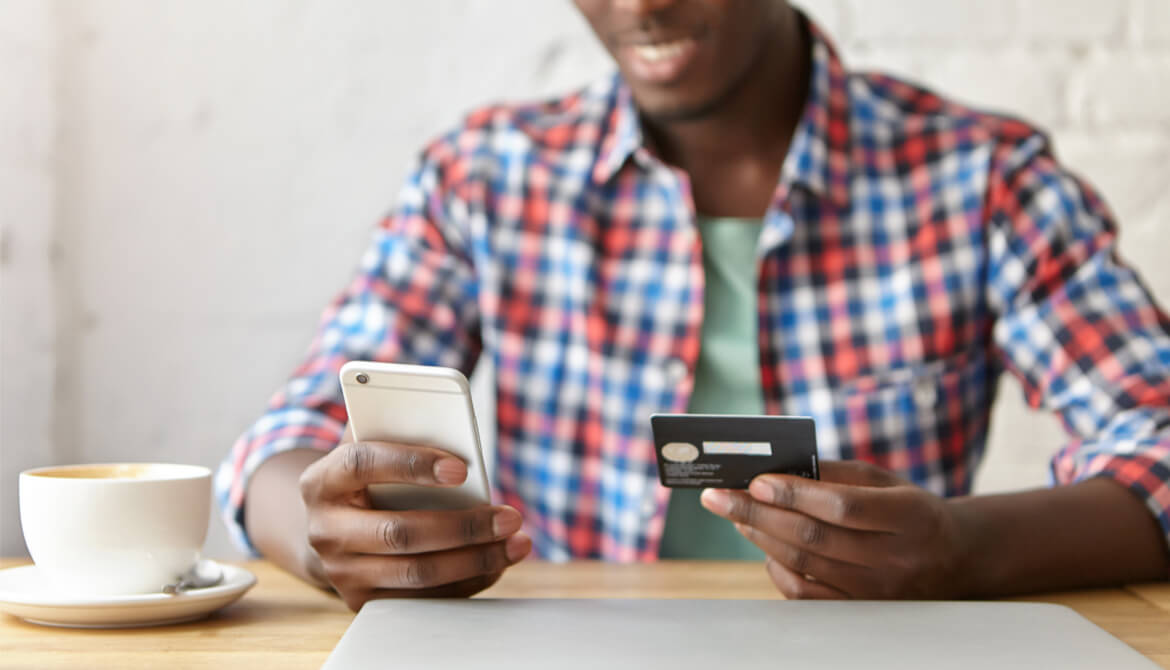 cheerful young African man using smartphone and credit card