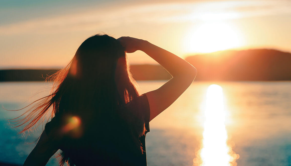 woman shields eyes while looking out over water at sun over horizon 