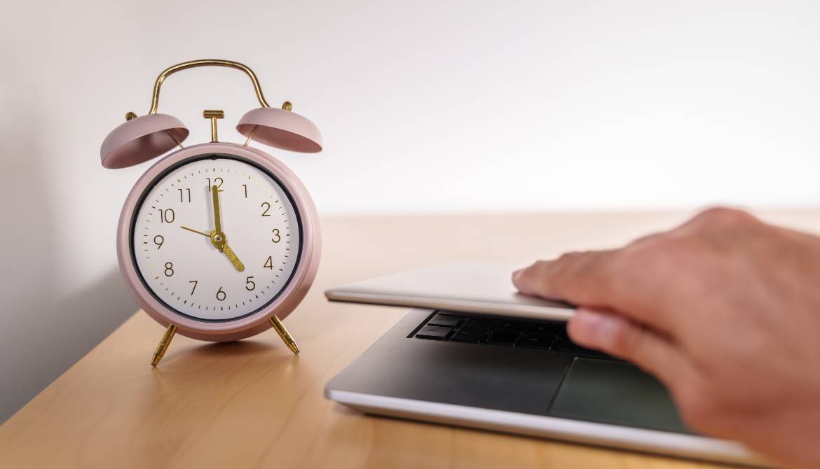 employee closes laptop on desk as alarm clock reaches 5 PM