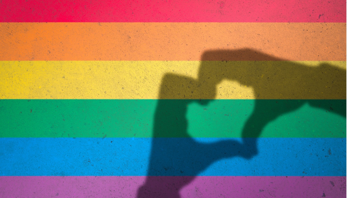 Hands making love heart shadow symbol of tolerance on gay pride rainbow colors painted on a textured concrete wall