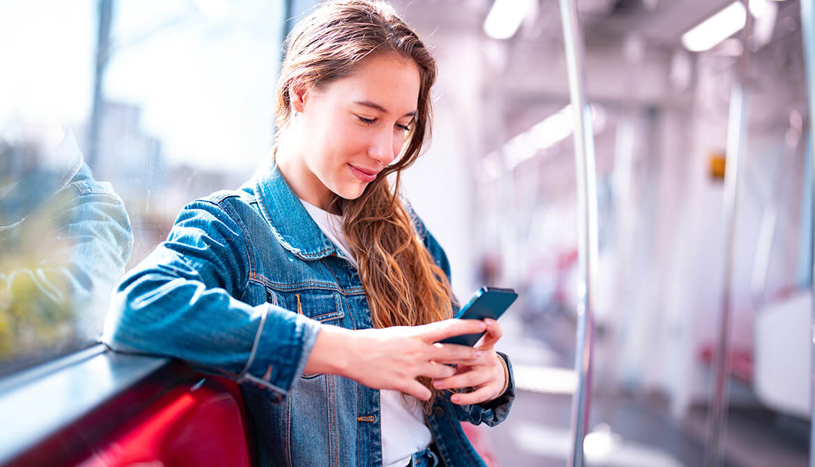 young woman looking at her smart phone while leaning on wall with window behind her