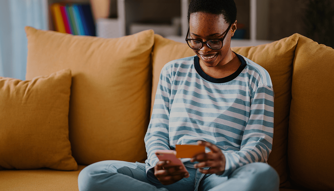 woman sitting on her couch looking at her smart phone and a business card