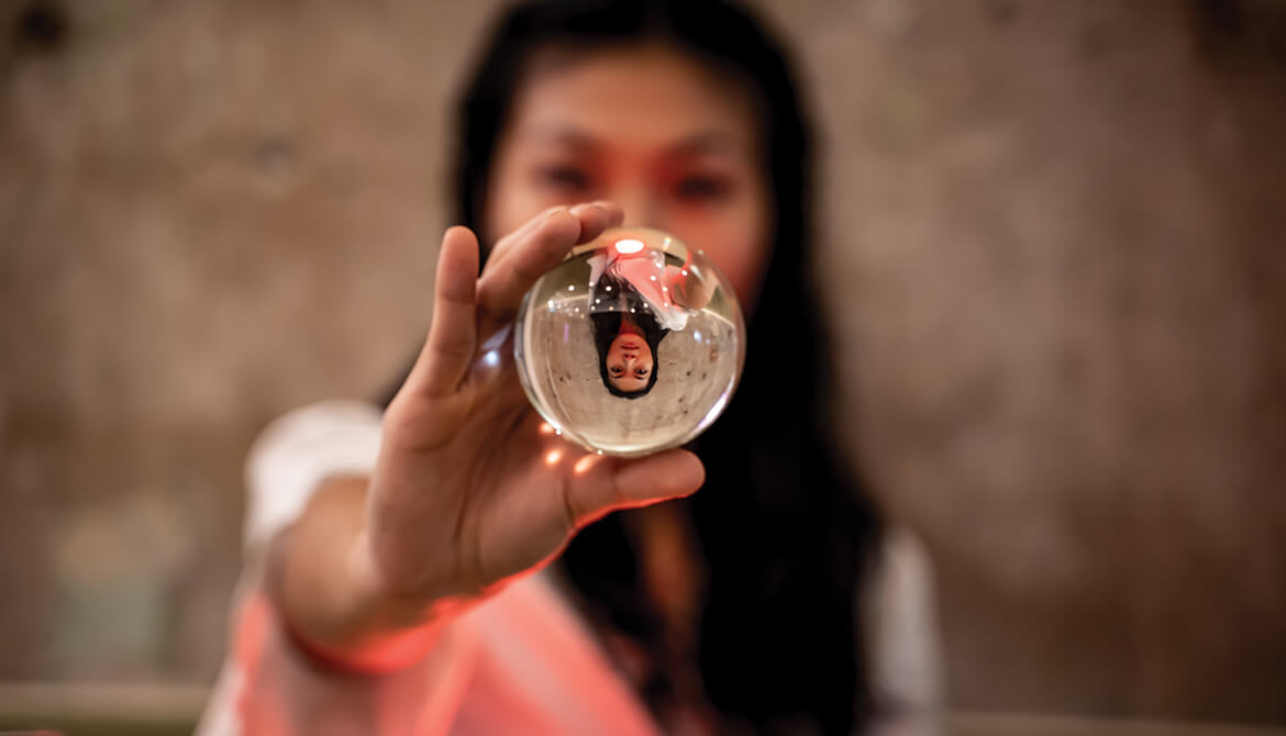 woman holding out glass ball with reflection of herself upside down within ball