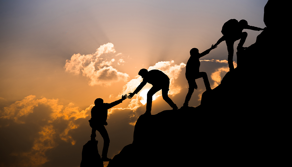 mountain climbers reach back to help the others up the climb