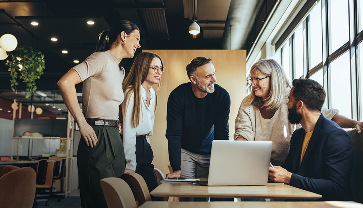 5 individuals standing around a table looking at a laptop