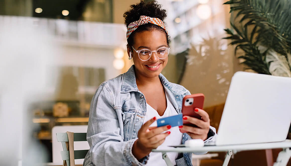 woman looking at her credit card and smart phone with big smile on her face