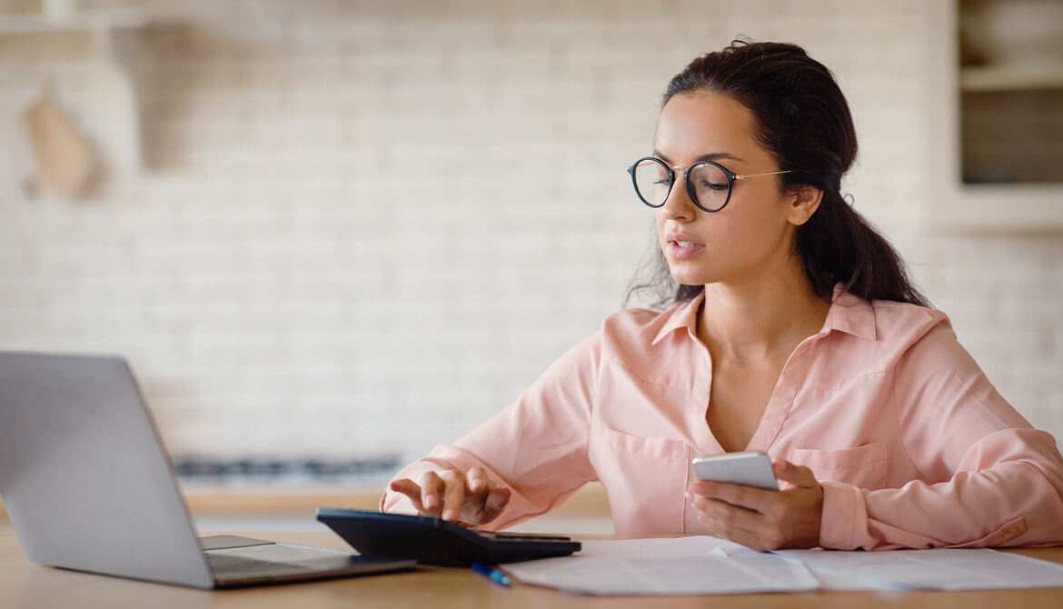 woman sitting in front of a laptop, calculator and smart phone