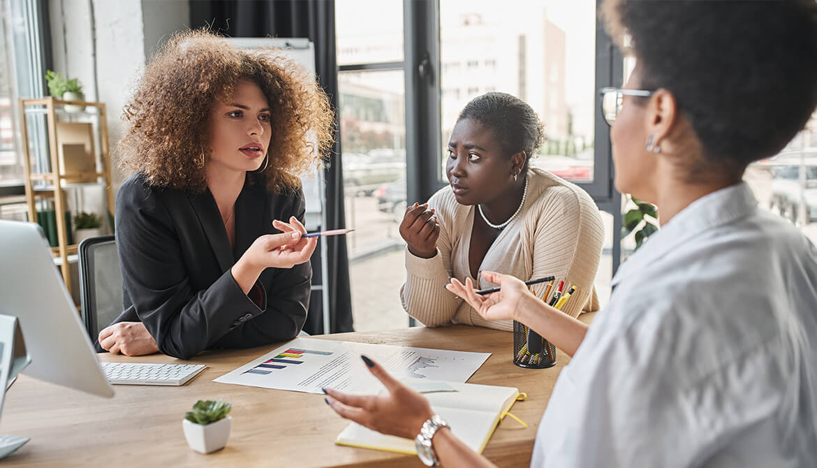 3 women having a discussion at a desk 