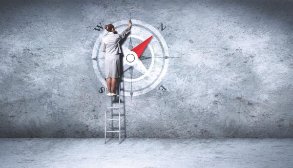 a woman on a ladder draws a compass on a gray wall