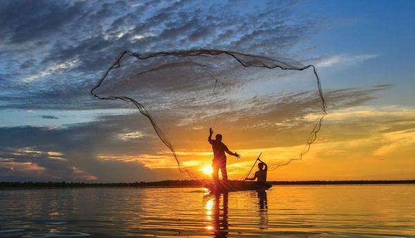two fishermen in rowboat casting a wide net into water