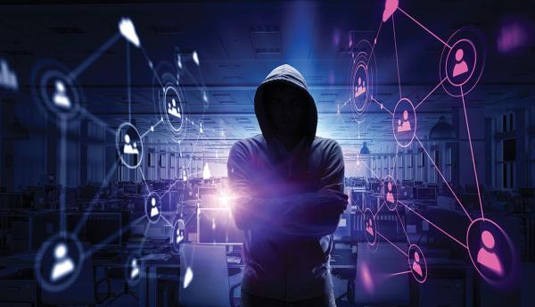 hacker in hoodie standing in darkened office full of computers with an image of a network of connected people floating in the background