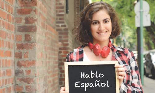 Young woman holding a chalk slate that reads Hablo Espanol