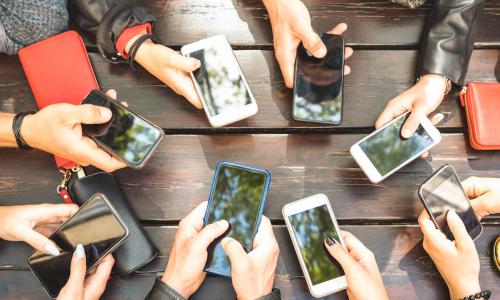 group of millennials' arms with phones around table