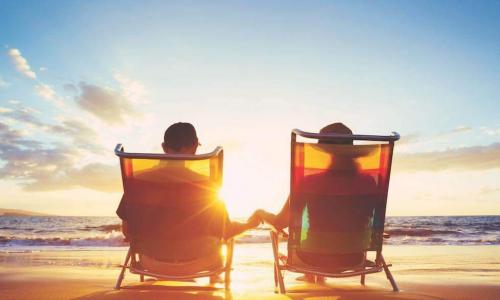 Retired couple sitting on chairs at the beach at sunset
