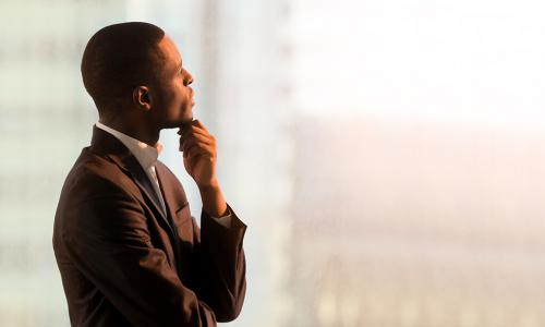 Portrait of pensive African-American businessman standing near window and thinking about decision