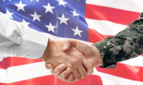 civilian and military arms shake hands in front of a U.S. flag