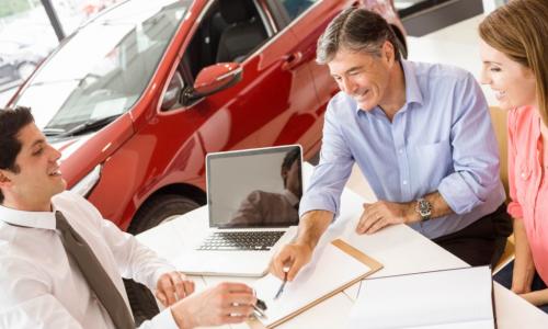 customers and car salesman at dealership desk signing papers
