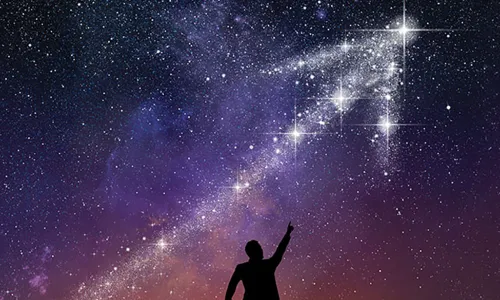 silhouette of a person pointing up at a galaxy in the shape of an upward arrow in the night sky