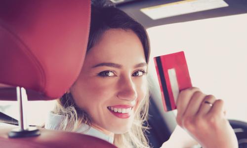 Happy woman sitting inside a new car and holding up her credit card