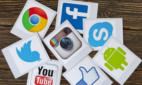social media icons printed on sheets of paper scattered on a wood surface