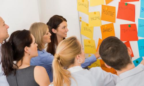 Business colleagues brainstorming multicolored labels stuck on whiteboard in meeting