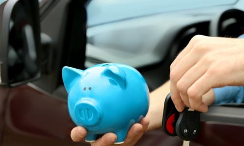 man holding blue piggy bank and car keys out car window
