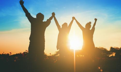 three people with their arms up to the sky with the glow of the sun