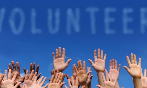 group of hands on a blue sky background with the word volunteer above them