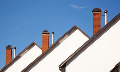three white houses with brick chimneys in a row against a blue sky