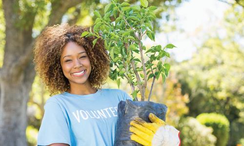 smiling African American woman wearing a volunteer t-shirt and holding a sapling ready to plant
