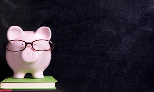 piggybank wearing glasses standing on a stack of books