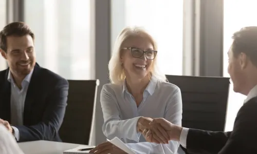 female director smiling and shaking hands with another board member
