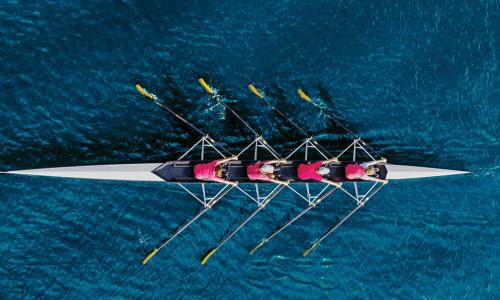 overhead view of rowing crew in red shirts moving through deep blue water