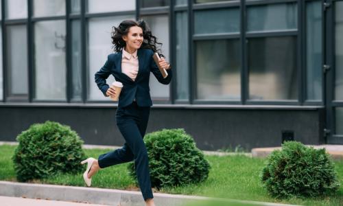 young happy businesswoman running to work in high heels with coffee and notebook