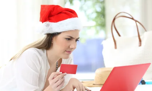 confused woman wearing a Santa hat using credit card with a red laptop