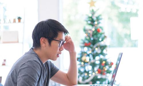 upset young main looks at his finances on laptop with Christmas tree in background