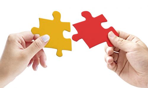 two hands putting together a red and a yellow puzzle piece