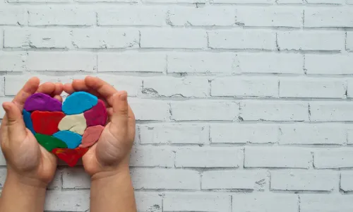 child’s hand holding multi-color, patchwork clay heart