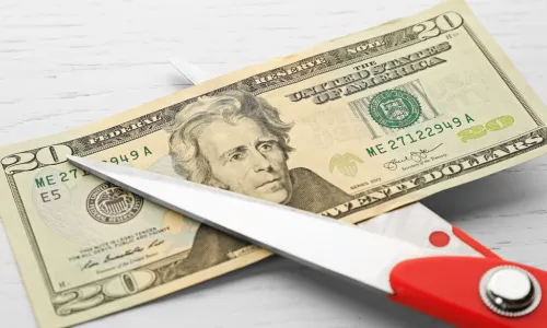 red scissors cutting twenty dollar bill