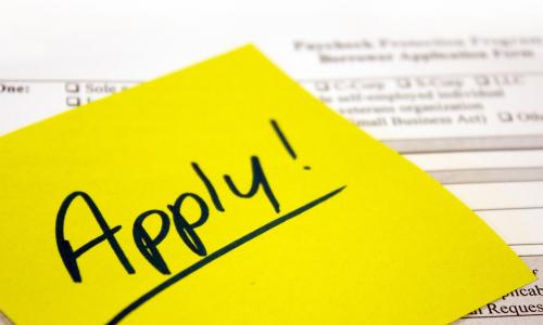 yellow sticky note with the word apply over a paycheck protection program loan application