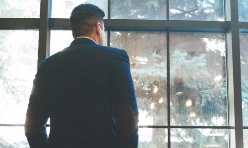 lone businessman in dark suit looks out window to courtyard