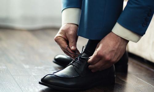 businessman in blue suit bending down to tie laces of black dress shoe