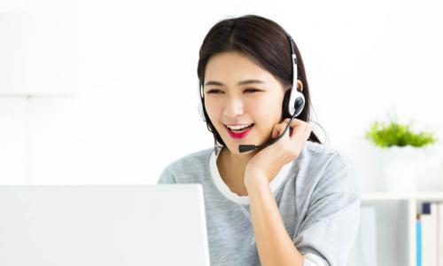 smiling service representative of Asian descent talks on headset while partipating in online training on laptop