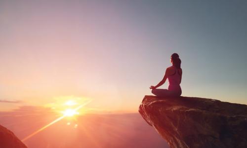 woman meditating on rock outcropping at sunrise