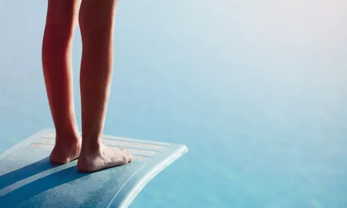 feet of person hesitating near edge of diving board above the water