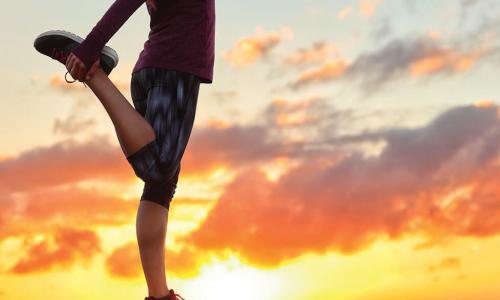 Runner stands on one leg while stretching at sunrise
